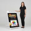 A woman standing next to the grand opening A-frame sign with her hand on the top of the sign