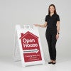 A woman standing next to an open house A-frame sign with her hand on the top of the sign