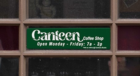 Green plastic sign with a coffee shop’s logo and open hours printed below
